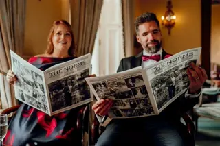 Two wedding guests reading The Norms wedding newspaper